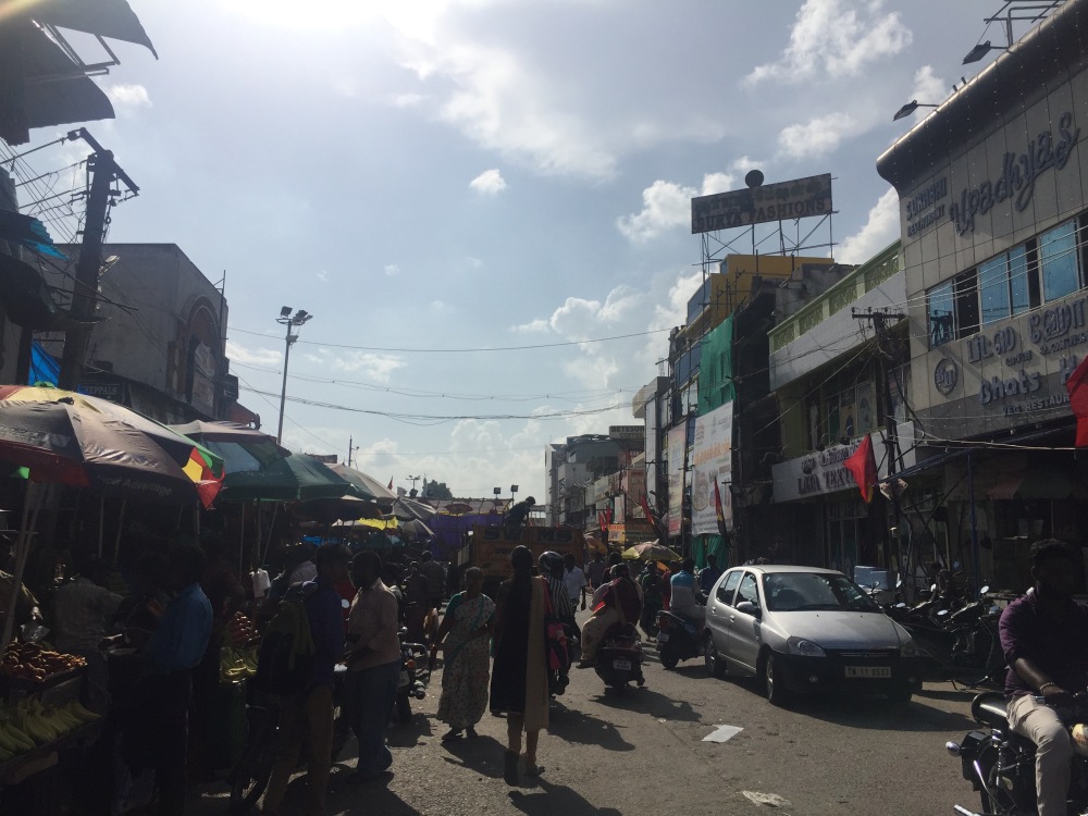 A busy street full of cars, people, bikers, and street vendors.
